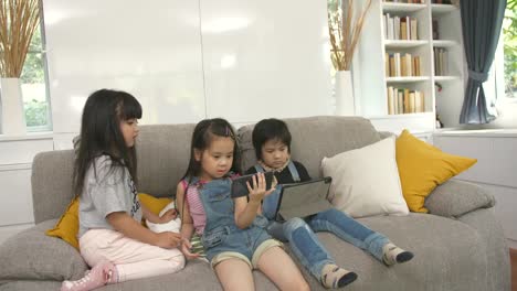 Group-of-kids-playing-with-digital-tablet-together-on-sofa-at-home,-and-smiling,-kids-on-digital-tablet-in-living-room.