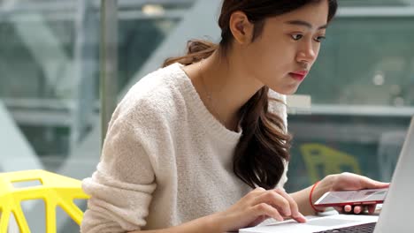 pretty-young-asian-woman-using-mobile-phone-and-laptop-indoor