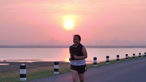 Übergewichtige-asiatische-Frauen-joggen-am-frühen-Morgen-im-Sonnenlicht-auf-der-Straße.-Konzept-des-Gewichtsverlustes-mit-Bewegung-für-die-Gesundheit.-zeitlupe