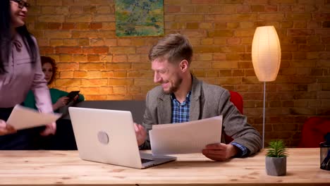 Closeup-shoot-of-adult-businessman-using-the-laptop-and-analyzing-graphs-indoors-in-the-office.-Female-secretary-bringing-him-a-cup-of-coffee