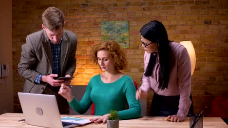 Closeup-shoot-of-three-employees-discussing-the-data-using-the-laptop-tablet-and-graphs-arguing-indoors-in-the-office