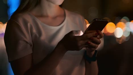 Close-up-de-un-teléfono-móvil-en-las-manos-de-una-chica-en-la-ciudad-por-la-noche