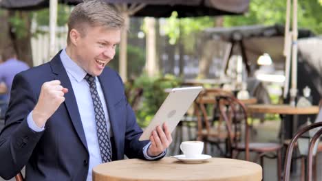 Empresario-celebrando-la-victoria-en-la-tableta,-sentado-en-la-cafetería-al-aire-libre