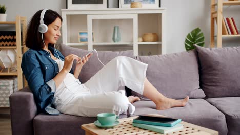 Dama-alegre-disfrutando-de-la-música-en-auriculares-tocando-la-pantalla-del-teléfono-inteligente-en-casa