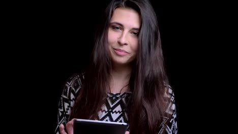 Closeup-shoot-of-young-pretty-caucasian-female-texting-on-the-tablet-then-looking-at-camera-and-smiling-with-background-isolated-on-black