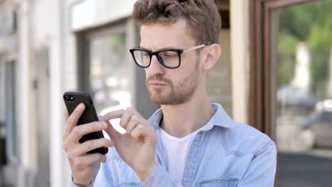 Hombre-joven-casual-usando-Smartphone-mientras-está-de-pie-al-aire-libre