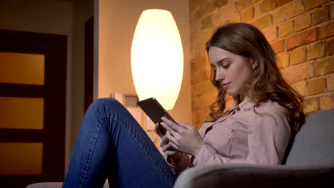 Portrait-in-profile-of-young-teenage-girl-typing-using-a-tablet-and-smiling-positively-in-cozy-home-atmosphere.