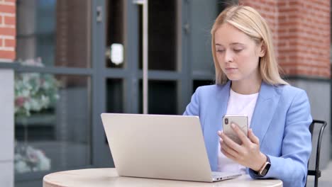 Young-Businesswoman-Using-Smartphone-and-Laptop,-Sitting-Outdoor