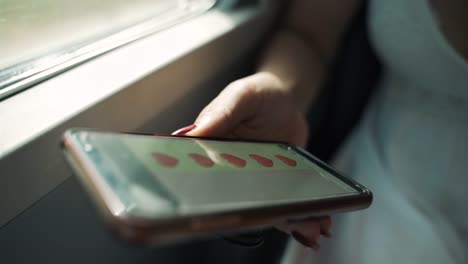 Primer-plano-de-la-mano-de-la-mujer-sosteniendo-el-teléfono-inteligente-moderno-y-charlando-con-su-novia-a-través-de-los-mensajes.-Enamorarse-chica-enviando-un-montón-de-corazones-rojos-en-sms-mientras-viaja-en-tren.-Pasajero-sentado-cerca-de-la-ventana