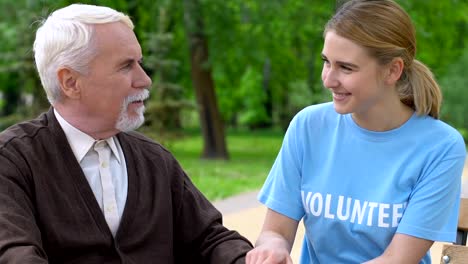 Joven-voluntario-sonriente-apoyando-a-ancianos-discapacitados-en-el-parque,-ayudando-a-jubilarse