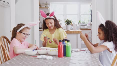 Gruppe-von-Mädchen-sitzen-um-Küchentisch-mit-Hasenohren-schmücken-Eier-für-Ostern---in-Zeitlupe-geschossen