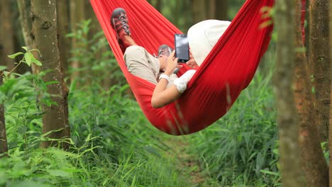 Mujer-relajándose-en-hamaca-con-teléfono-inteligente-en-la-selva-tropical,4k