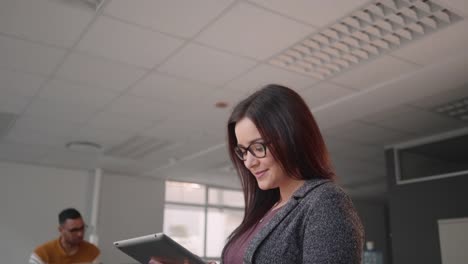 Tilt-up-shot-of-a-successful-happy-young-businesswoman-searching-data-on-digital-tablet-and-her-business-team-talking-with-each-other-at-background