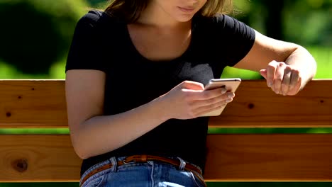 Young-lady-scrolling-social-networks-on-smartphone,-relaxing-on-park-bench,-app