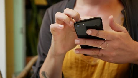 Happy-girl-uses-a-smartphone,-writes-a-message,-chatting.-Young-woman-looking-for-information-in-the-phone.-Sitting-in-restaurant-with-friends.-Breakfast-time