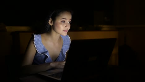 Joven-hermosa-mujer-asiática-sonriendo-mientras-usa-el-ordenador-portátil-en-la-habitación-oscura