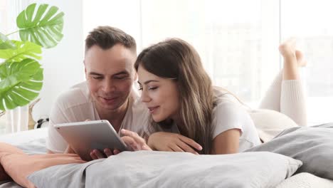 Couple-using-digital-tablet-lying-on-bed