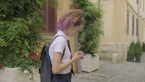 Hermosa-estudiante-adolescente-chica-con-teléfono-inteligente-leer-y-escribir-mensaje-de-texto,-sonriendo-en-la-calle-de-la-ciudad