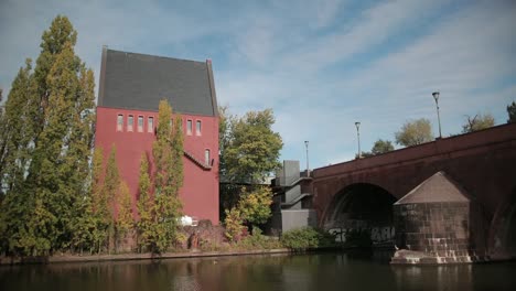 Hermosa-casa-alta-roja-en-el-lado-opuesto-del-río,-un-antiguo-puente-sobre-el-estanque.