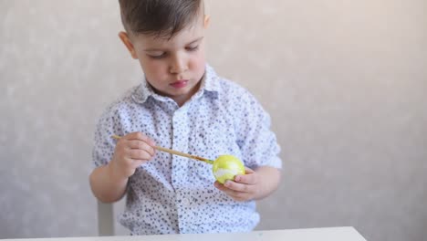 Un-niño-pinta-un-huevo-de-pascua-en-la-mesa-sobre-un-fondo-blanco.