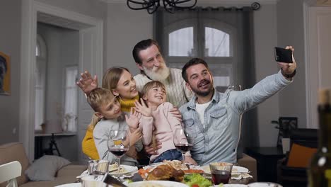 Attractive-happy-family-waving-hands-while-making-selfie-at-the-family-feast