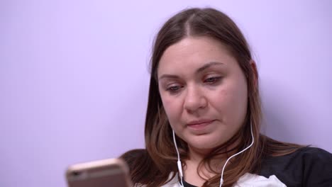 Young-girl-is-smiling,-sending-messages-and-talking-on-mobile-phone-using-video-calling-and-headset-or-listening-to-music-with-headphones-in-the-app-on-smartphone.-Female-freelancer-works-at-home