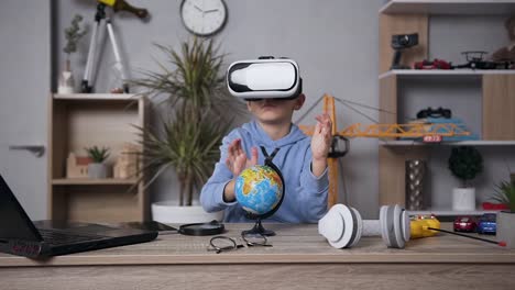 Atractivo-niño-concentrado-de-6-años-sentado-en-la-mesa-en-su-habitación-y-se-tachando-la-estructura-del-globo-usando-gafas-virtuales-especiales-en-3D