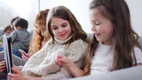 Gruppe-von-Kindern-mit-Freunden-sitzen-auf-dem-Sofa-zu-Hause-spielen-zusammen-auf-digitalen-Geräten