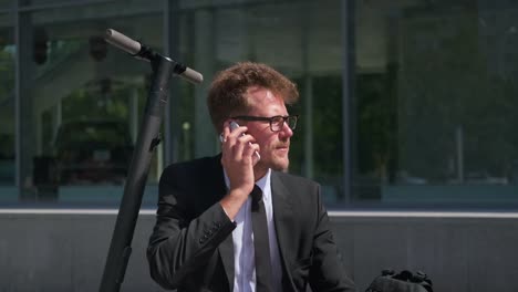 Office-worker-talking-on-cellphone-sitting-on-electric-scooter-outdoors