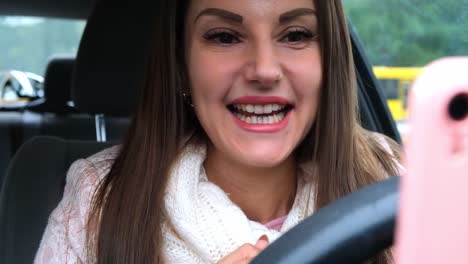 Mujer-alegre-usando-un-teléfono-inteligente-en-un-coche-de-conducción.-Retrato-de-una-mujer-alegre-mirando-el-teléfono-mientras-conduce