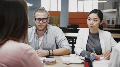 Junges-Team-von-multirassischen-verschiedenen-Kollegen,-die-während-des-Brainstormings-eine-Strategie-für-ein-Startup-Projekt-entwickeln,-am-Tisch-im-Büro-sitzend