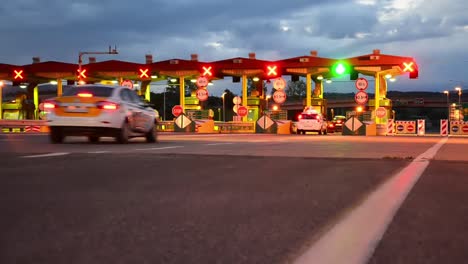 Lapso-de-tiempo-de-carretera-coche-Paytoll-al-amanecer,-luces-de-la-noche-y-Autos-pasando-por-cabinas-de-peaje,-pagar-por-usar-la-carretera-y-autopista