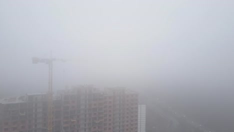 Aerial-view.-A-multi-storey-brick-house-in-the-city-in-a-fog.-A-construction-crane-is-installed-on-the-site-of-the-construction-of-a-residential-building.-New-homes-for-sale-and-rent-of-real-estate