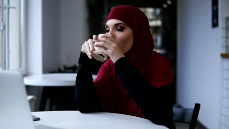 Attractive-female-with-unbelievably-beautiful-eyes-and-hijab-is-drinking-cappuccino.-Indoors-footage