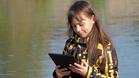 The-child-with-the-tablet-is-talking-on-skype.-Little-girl-in-the-nature-with-a-tablet