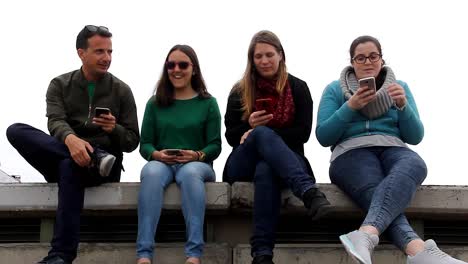 Drei-Frauen-und-ein-Mann-mit-Handys-sitzen-auf-Tribünen-an-bewölkten-Tag