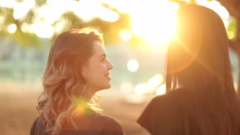 Chica-mirando-a-su-amiga-durante-puesta-del-sol-dorado-del-atardecer-hora-con-sunklight-llamarada.-Amigas-juntos-en-el-Parque