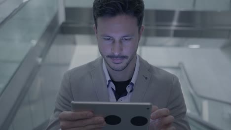 Guapo-joven-empresario-escribiendo-textos-sobre-tableta-digital-en-el-espacio-público