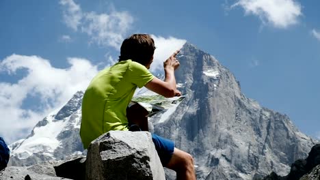 Turismo-hombre-caminante-mirando-el-mapa-y-estudiar-la-ruta-en-la-montaña-sentado-en-la-cerca-de-piedra,-cámara-lenta