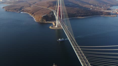 Great-aerial-view-of-ferry-floating-under-Russian-bridge,-and-Russian-island