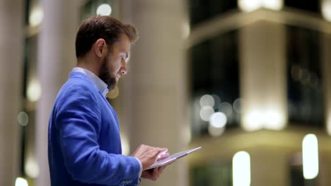 Seitenansicht-des-gut-aussehender-Mann-in-blauer-Jacke-mit-Tablet-Computer-im-Freien-im-Abend