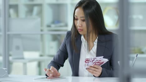 Businesswoman-Counting-Chinese-Banknotes-and-Calculating-on-Digital-Tablet