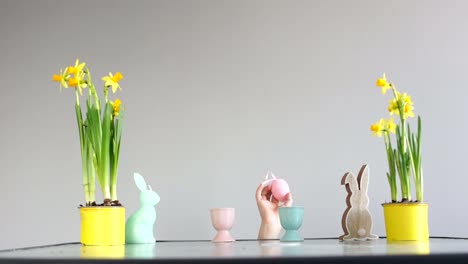 Decoración-de-Pascua-en-la-mesa.-Las-manos-de-los-niños-secuestran-huevos-adornados.-Narcisos-en-maceta,-estatuilla-del-conejo