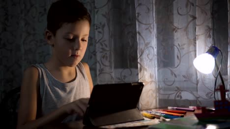 Niño-utiliza-tableta-para-estudiar,-niño-escribiendo-tarea-en-la-noche-uso-de-Internet-FullHD