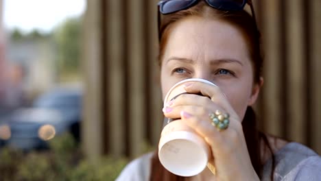 Schöne-junge-kaukasische-Frau-sitzt-nach-der-Arbeit-am-Abend-in-einem-Straßencafé-beim-Kaffee-und-plaudert-in-sozialen-Netzwerken-mit-einem-Smartphone.