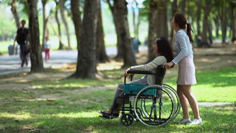 Hübsche-Teenager-Tochter-und-Mutter-auf-Rollstuhl-im-Park