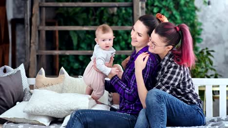 Two-happy-same-sex-parents-smiling-playing-with-little-infant-daughter-enjoying-weekend