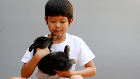 Joven-niño-Asiático-está-jugando-con-el-conejo-negro-encantador