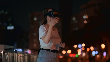 Junge-Frau-in-Virtual-Reality-Brille-in-der-Nachtstadt-bewegt-ihre-Hände