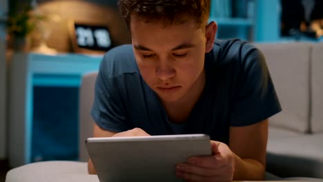 A-teenager-is-lying-on-the-couch-on-his-belly-and-playing-on-a-tablet